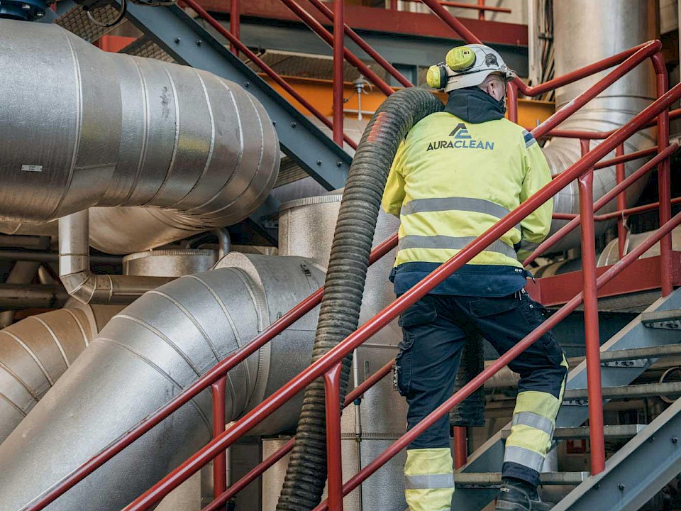 Auracleanin työntekijä vetää suurtehoimurin imuletkua teollisuuslaitoksessa
